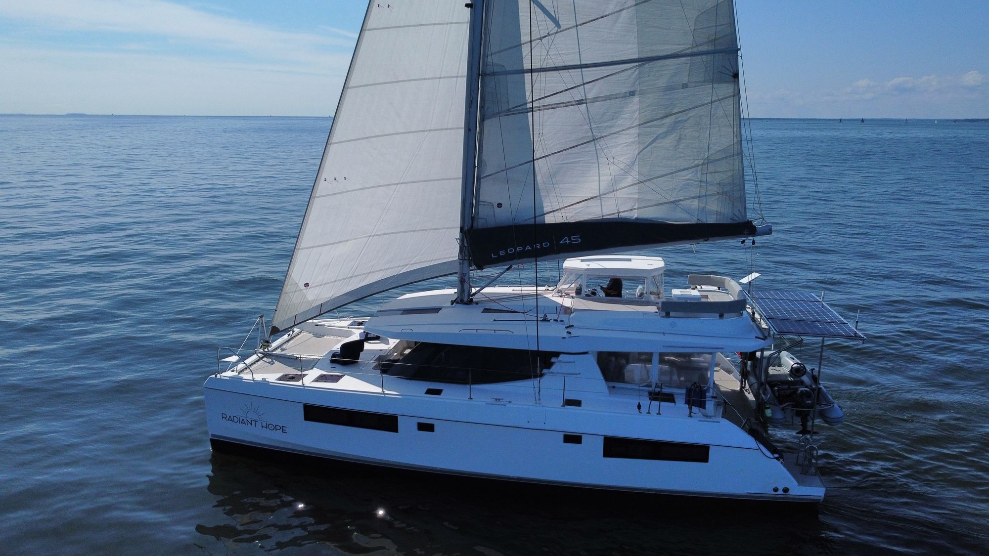 Radiant Hope under sail on the Chesapeake, port beam view with solar arch and tender visible